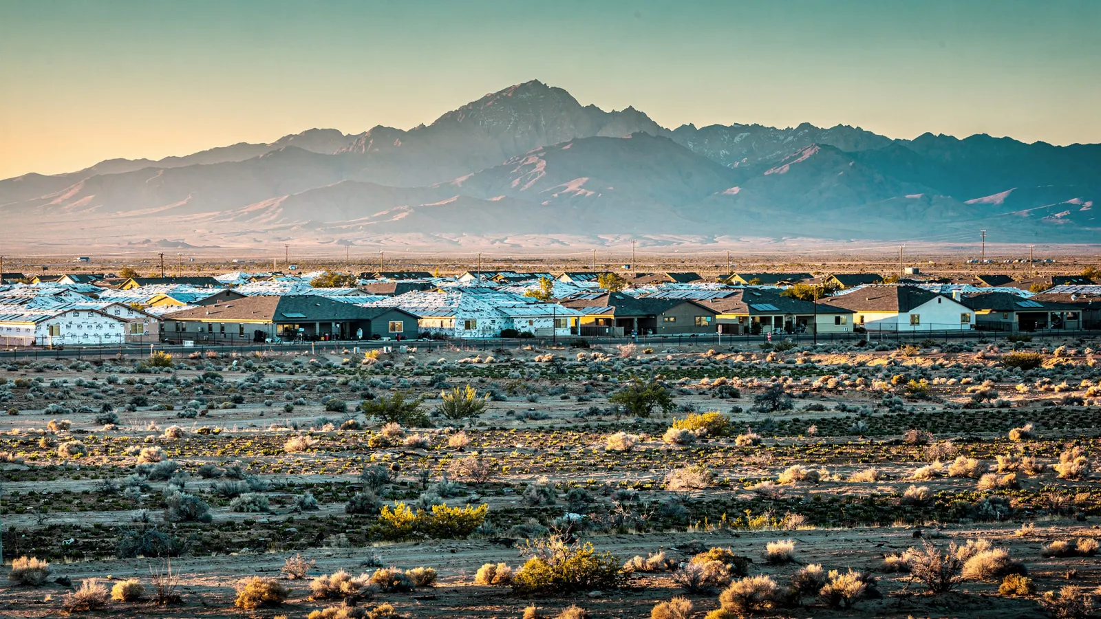 Open desert farmland near Buckeye with new rooftop subdivisions and the White Tank Mountains
