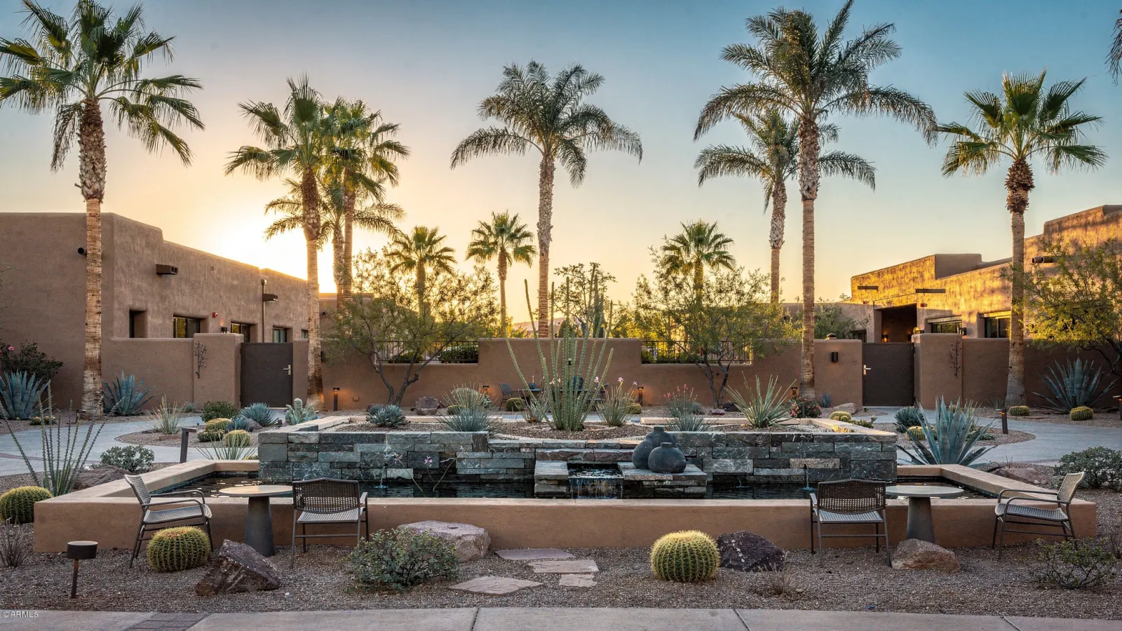 Upscale Scottsdale resort plaza with palm trees, a stone water feature and adobe architecture