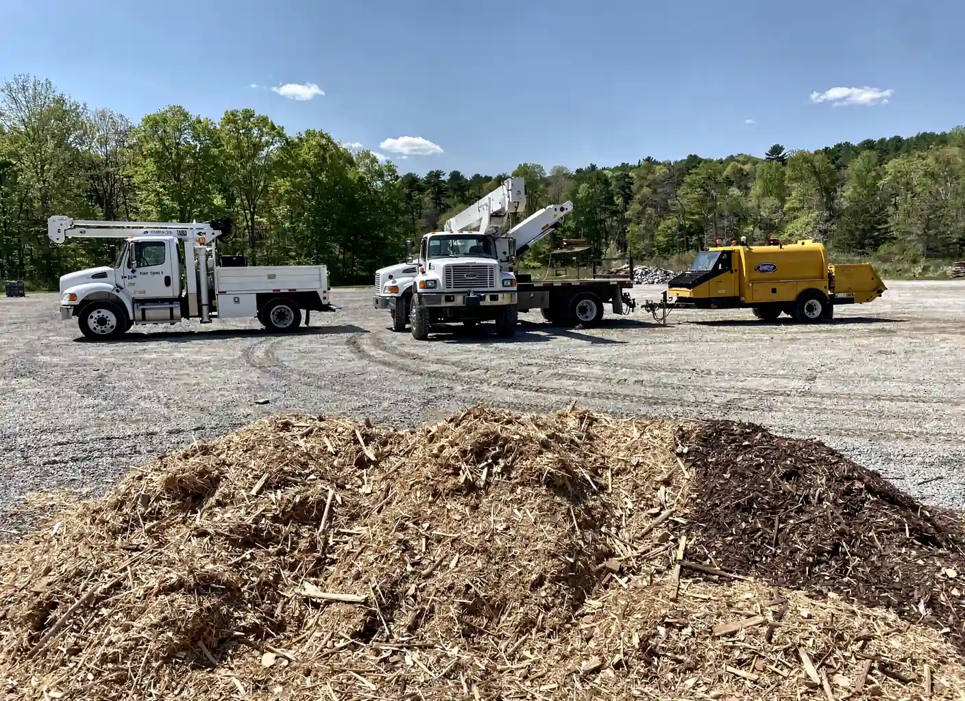 Company equipment lineup: bucket truck, crane truck, chipper and mulch pile
